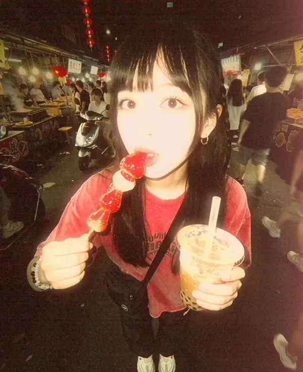 A girl eating at a night market, lit by flash against a dark street.